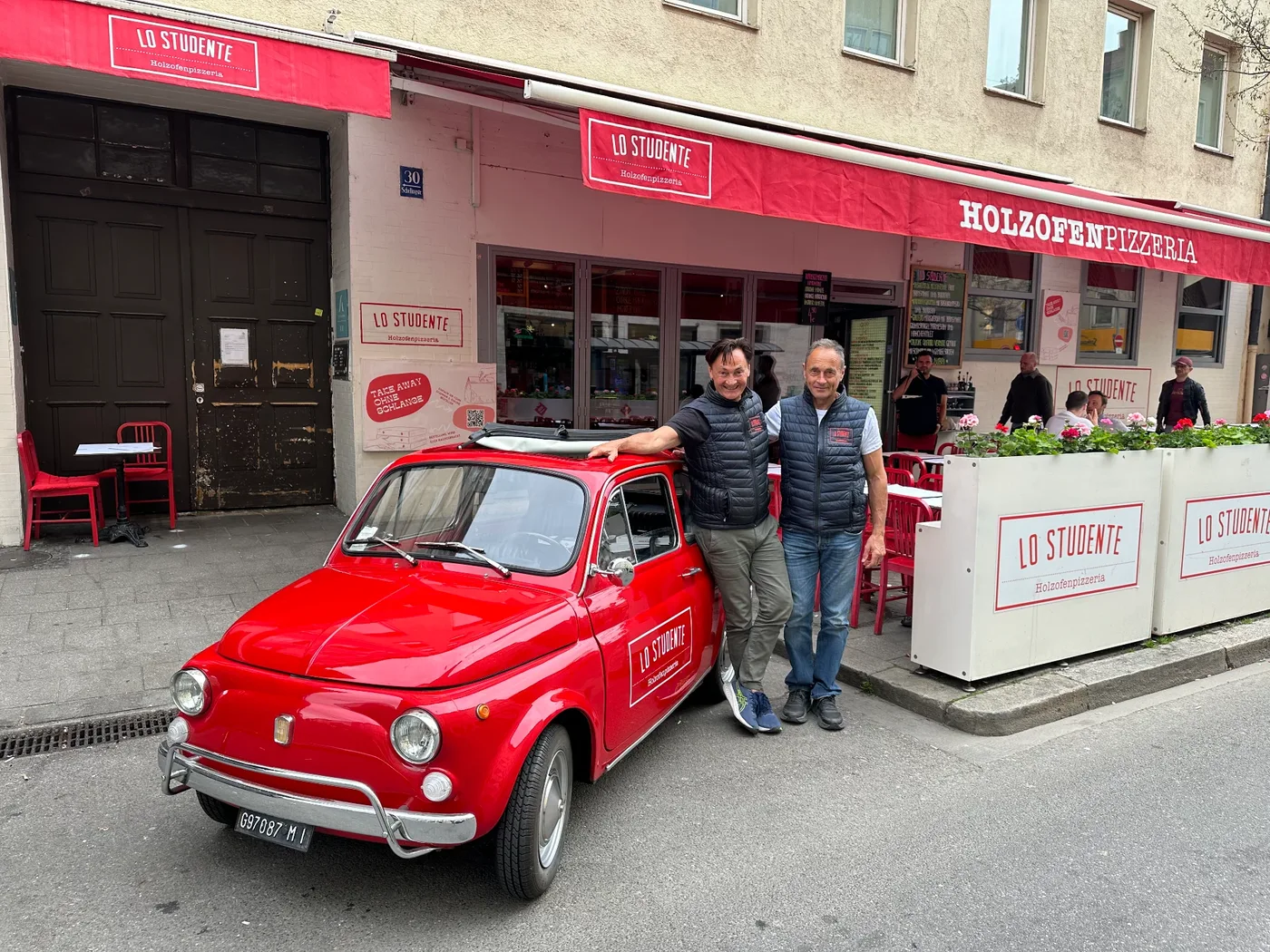 Euer Lo Studente Team steht lächelnd mit dem roten Fiat 500 vor dem Restaurant in der Schellingstraße