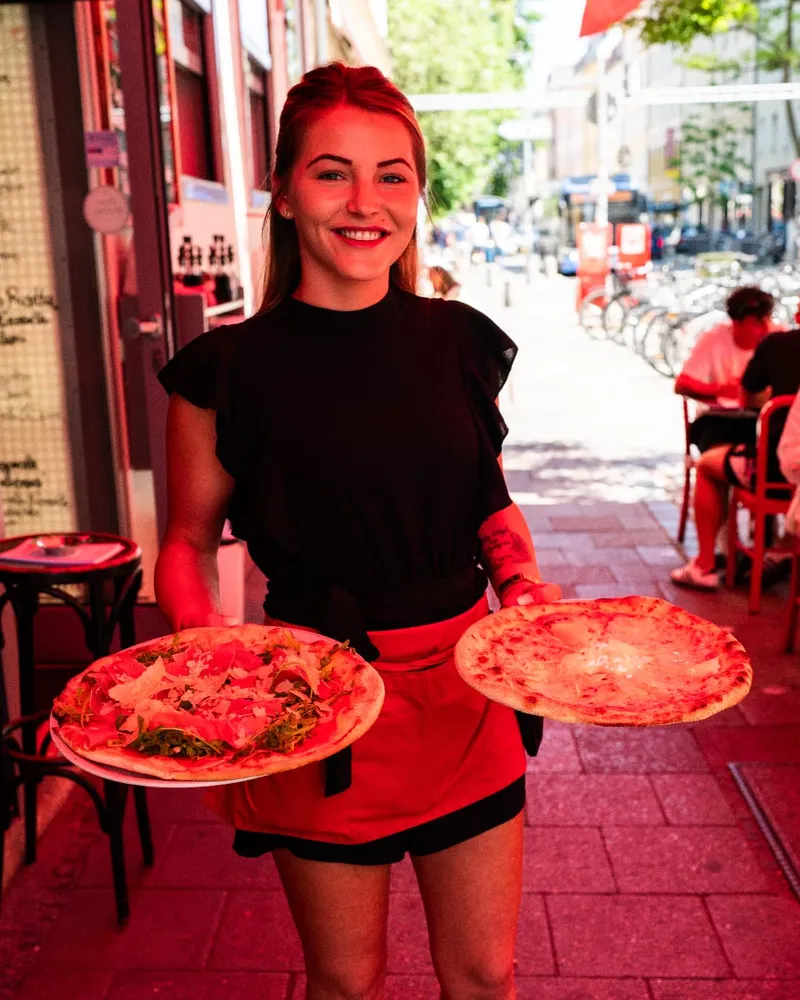 Servicekraft bringt zwei frische Pizzen vor dem Restaurant